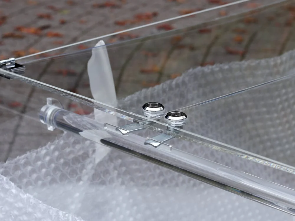 Close-up of through-bolted metal hinges and twin cam locks on the clear acrylic lid